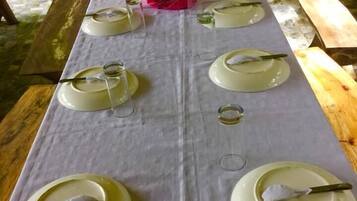 A table set for six with white plates, cutlery, and glasses, surrounded by natural greenery.