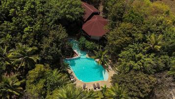 An aerial view of a resort with a central swimming pool surrounded by lush greenery and palm trees.