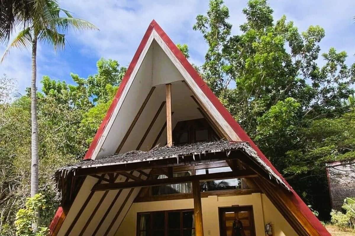 Une petite maison au toit triangulaire, dotée d’un porche, de meubles en bois et d’une porte.