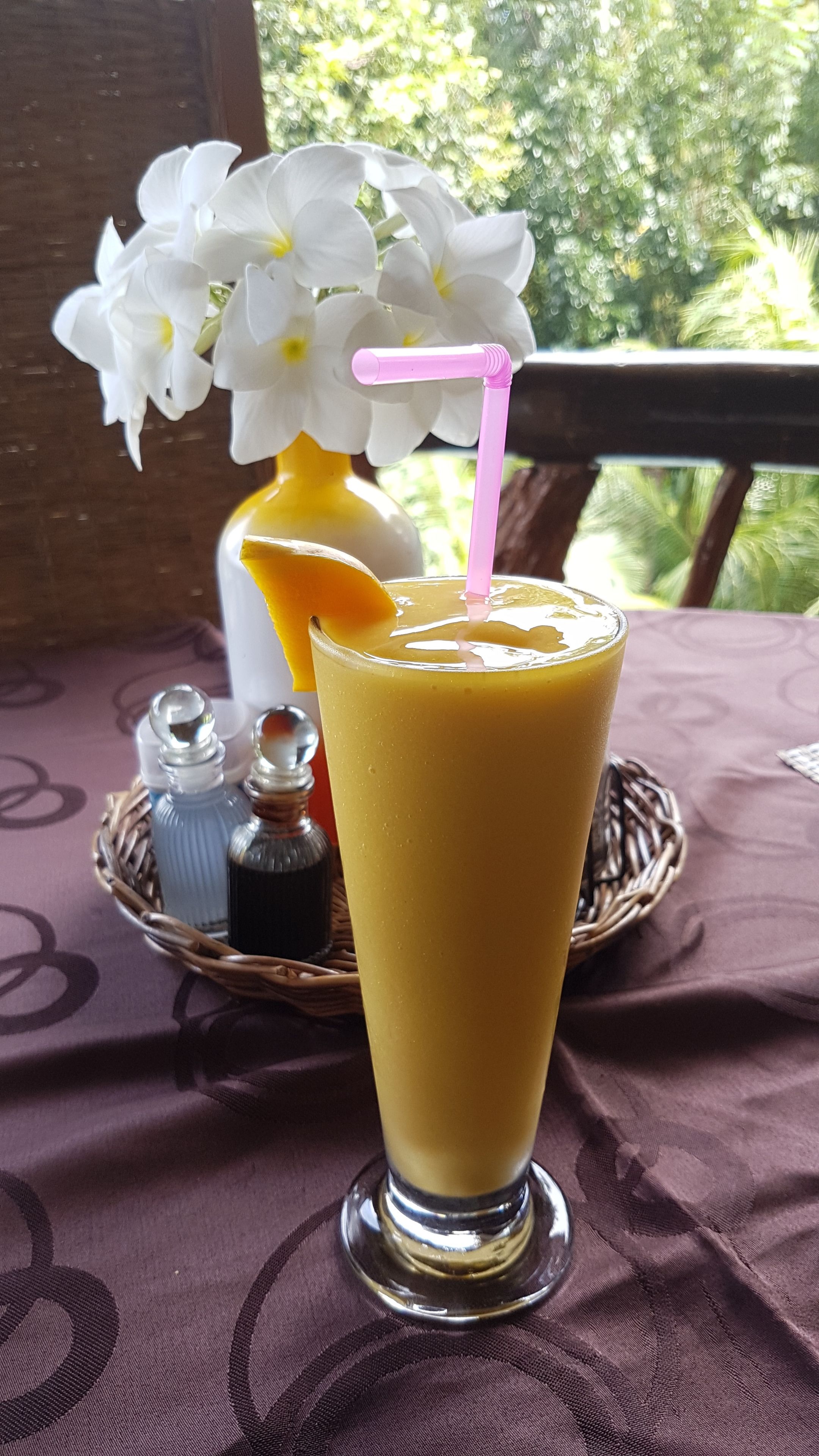 A glass of orange juice with a pink straw on a table with a purple tablecloth.