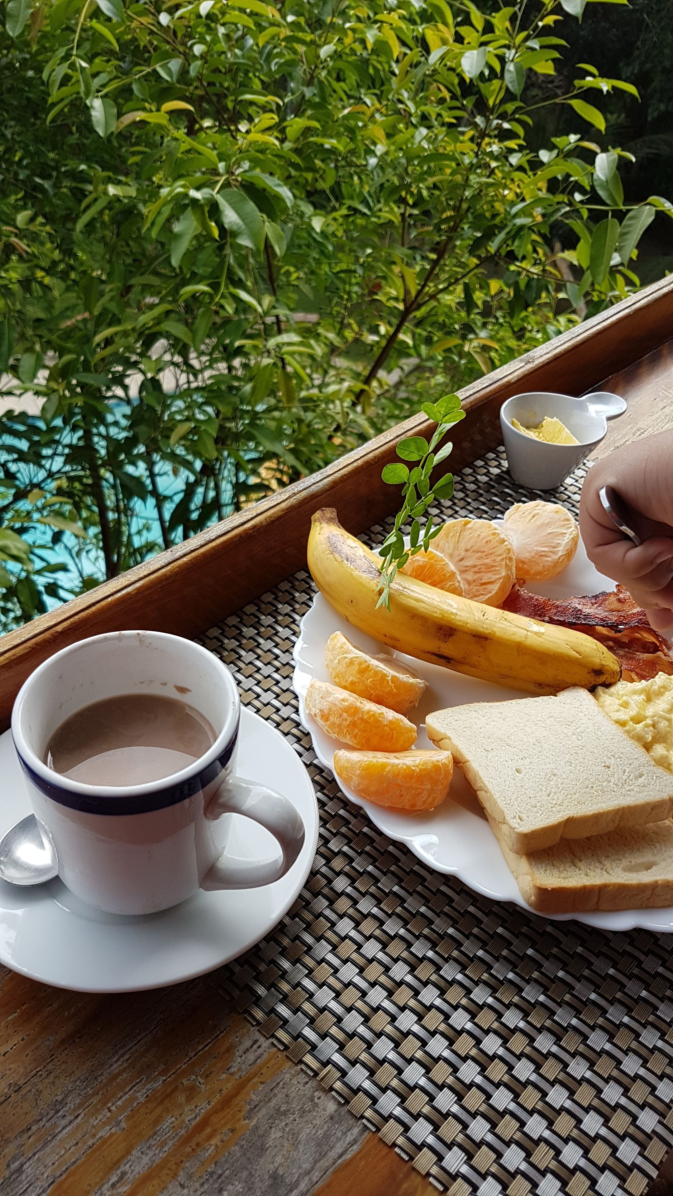 Un vassoio con prodotti per la colazione, tra cui pane tostato, uova, pancetta, una banana e arance, accompagnato da una tazza di caffè.