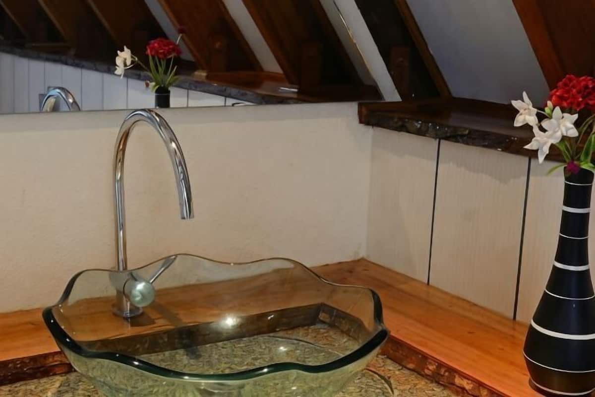 Un lavabo en verre, doté d’un robinet moderne, un plan de travail en bois et un vase rempli de fleurs.