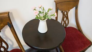 A round table with a white vase containing pink flowers, surrounded by two wooden chairs with red cushions.