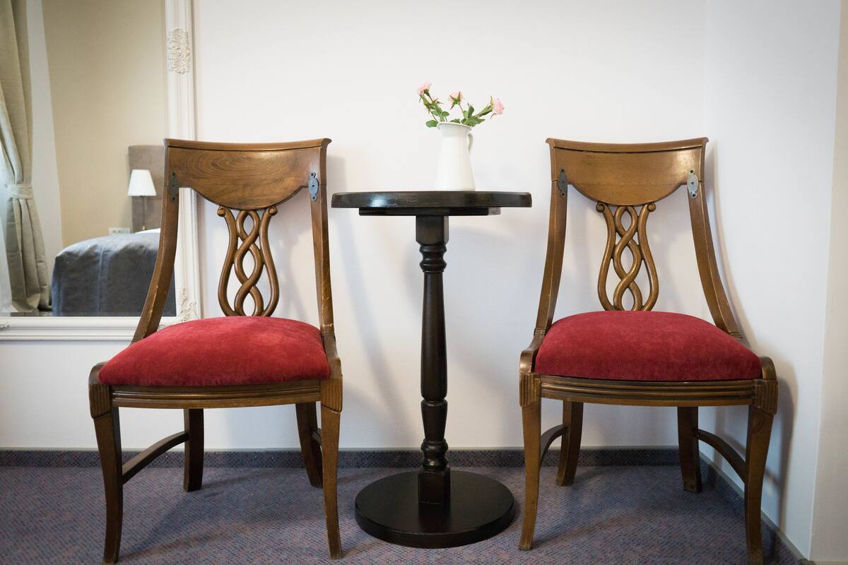 Two wooden chairs with red cushions and a small table with a vase of flowers between them.