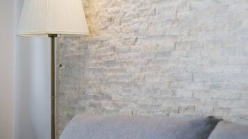 A lamp with a white shade and a wall-mounted light fixture against a textured brick wall.