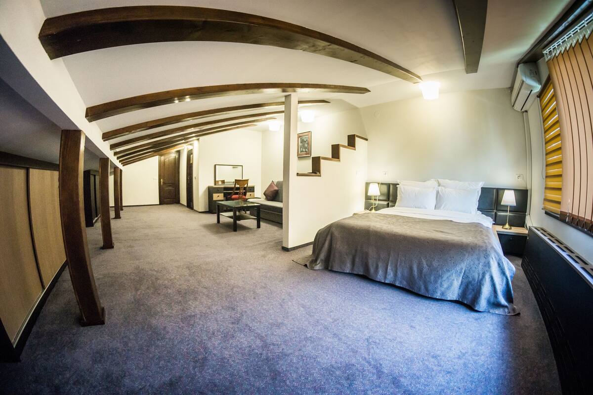 A hotel room with a bed, a desk, a chair, a nightstand, and a staircase leading to another room.