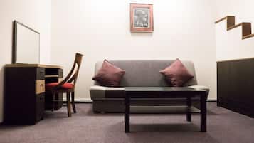 A room with a grey sofa, two red cushions, a wooden chair, a black table, and a framed artwork on the wall.