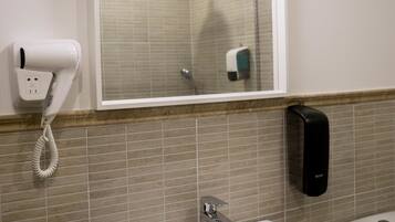 A bathroom with a white sink, a mirror above it, a hairdryer on the wall, and a hand dryer.