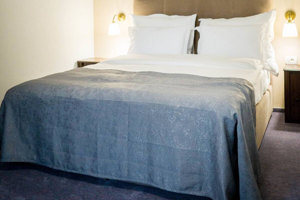A hotel room with a large bed, wooden beams on the ceiling, and two bedside lamps.