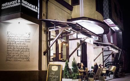 An outdoor cafe with tables and chairs, a signboard with text, and a building entrance.