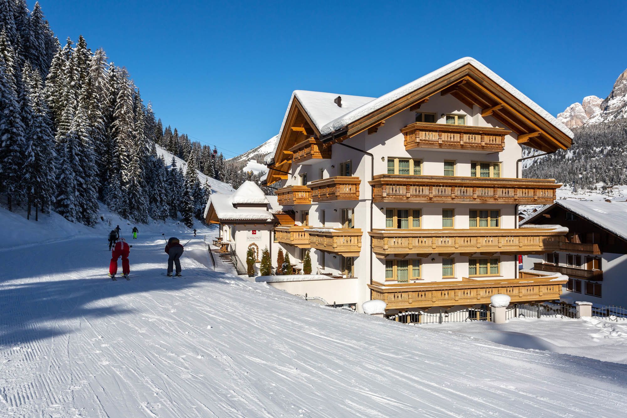 A multi-story chalet with wooden balconies and a ski slope in the background.