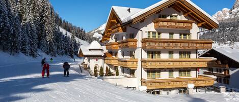A multi-story chalet with wooden balconies and a ski slope in the background.