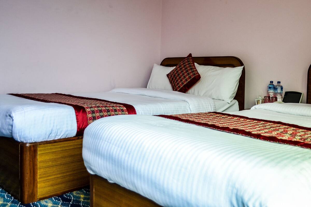 Dos camas individuales con estructura de madera, ropa de cama blanca y colchas estampadas en rojo.