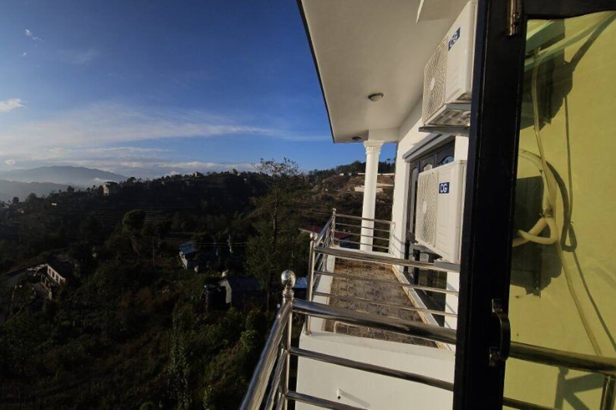 Vista desde un balcón sobre un valle, cielo despejado y montañas a lo lejos.