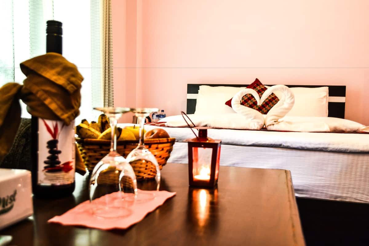 Una habitación de hotel con una cama bien hecha, una mesita de noche con una botella, vasos y un farol.