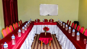 Un salón de conferencias con una larga mesa, sillas rojas, botellas de agua y una pizarra en la pared.