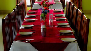 Una larga mesa de comedor dispuesta para una comida, con manteles rojos, platos blancos y un jarrón de flores.