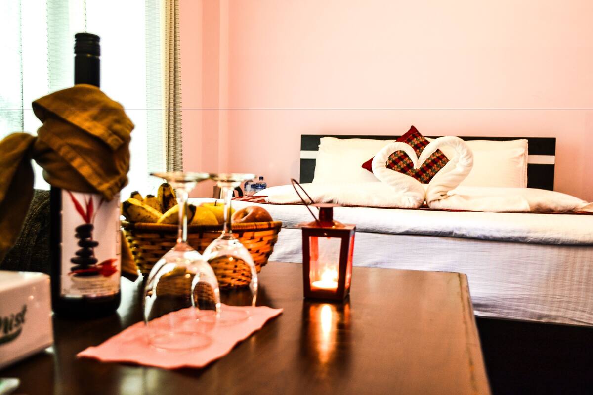 Una habitación de hotel con una cama bien hecha, una mesita de noche con una botella, vasos y un farol.