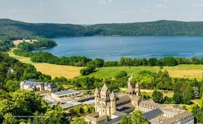 A historic building with multiple towers and a large body of water in the background. - Seehotel Maria Laach (Glees)
