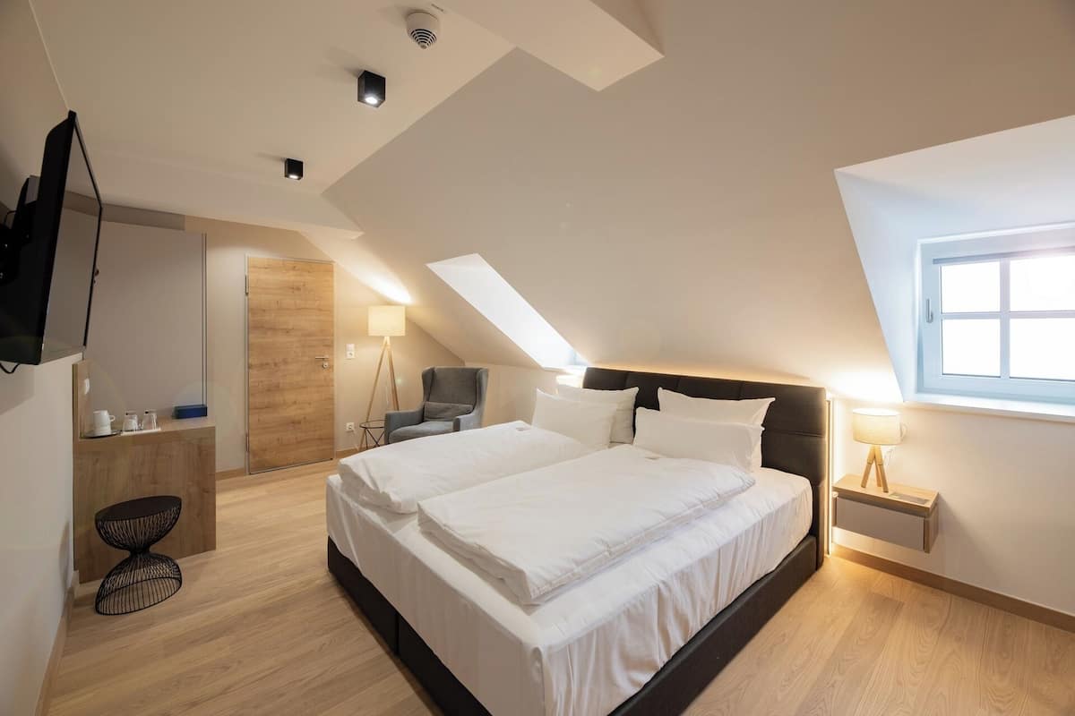 Ein modernes Hotelzimmer mit einem großen Bett, einem Schreibtisch, einem Sessel und einem Fernseher.