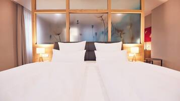 A hotel room with a large bed, two bedside lamps, a wooden headboard with frosted panels, and a large window with a view of trees.