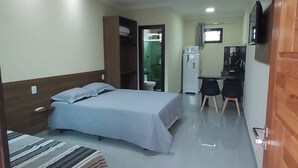 A hotel room with two beds, a desk with a chair, a small refrigerator, and a television on the wall. - Praia do Foguete Style (Cabo Frio)