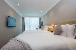 A modern hotel room with a large bed, a flat-screen TV mounted on the wall, and a window with curtains. - Luxury Apartment Ocean View (Da Nang)