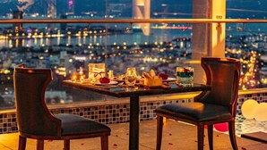 Une table avec deux chaises, placée sur un balcon donnant sur une vue panoramique de la ville la nuit.