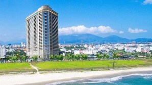 Un hôtel de grande hauteur au design moderne, situé près d’une plage aux eaux cristallines et offrant une vue sur les montagnes lointaines.