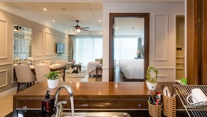 Une chambre d’hôtel avec une coiffeuse en bois, un lavabo, un ventilateur de plafond, un coin repas avec des chaises et une table, et un lit donnant sur l’extérieur.
