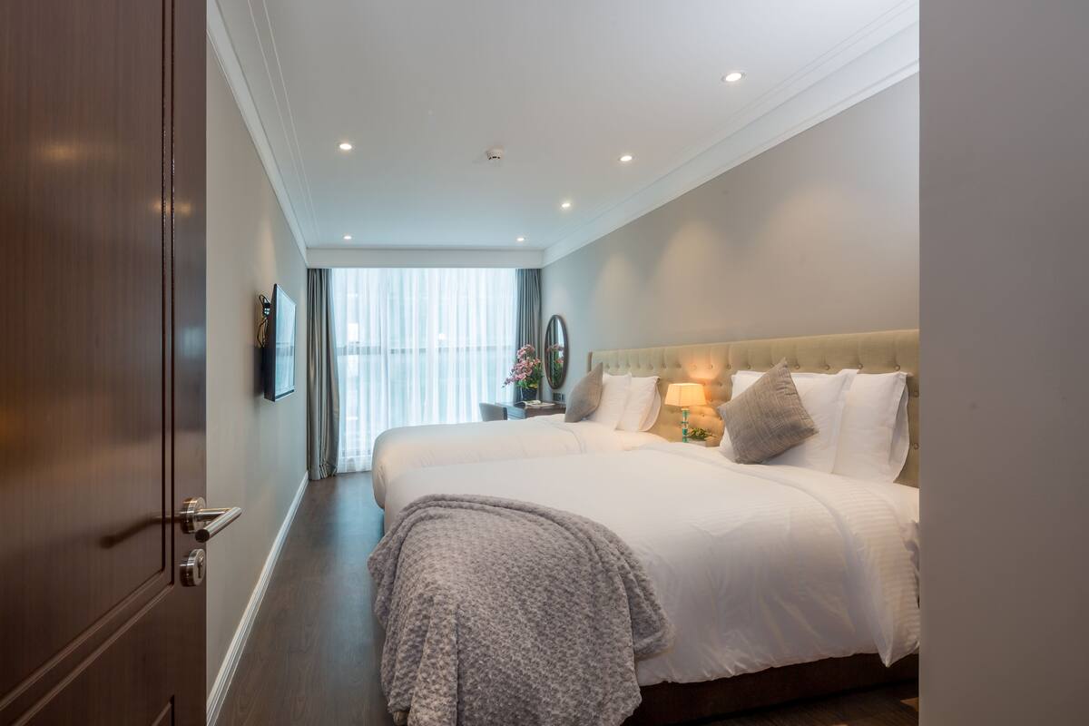 A hotel room with a large bed, a television, and a window with curtains.