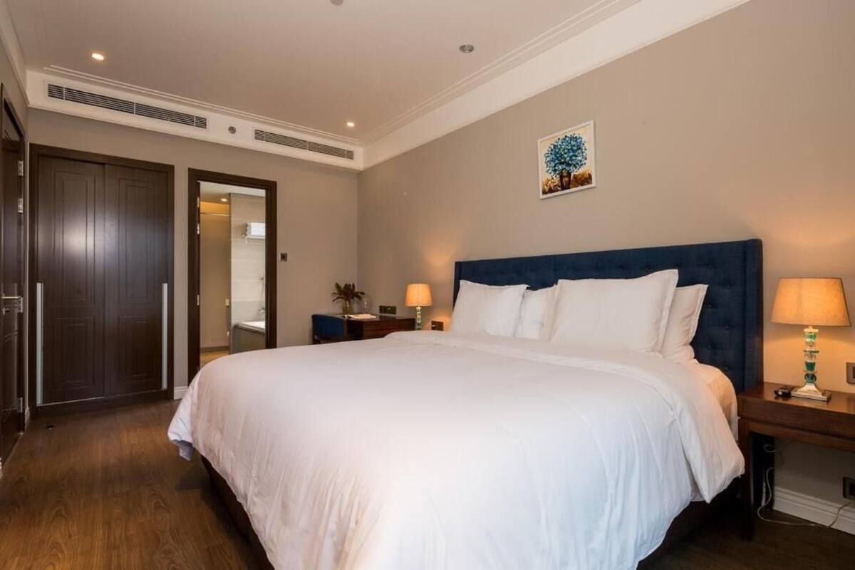 A neatly arranged bedroom with a large bed, bedside tables, and a door leading to another room.