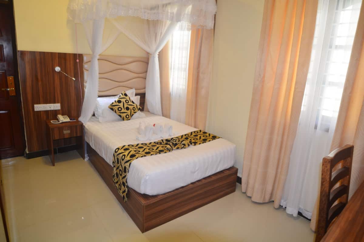 Quarto de hotel bem arrumado, com cama, mesa de cabeceira e criado-mudo.