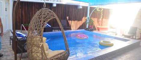Un área de piscina con una hamaca colgante, sillas de descanso y un dosel azul.