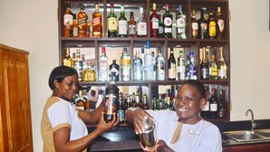 Dos bartenders preparando bebidas en un bar con una variedad de botellas de licor en las estanterías.