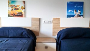 Habitación de hotel con dos camas, cabecera de madera y obra de arte que muestra un coche y una escena de playa.