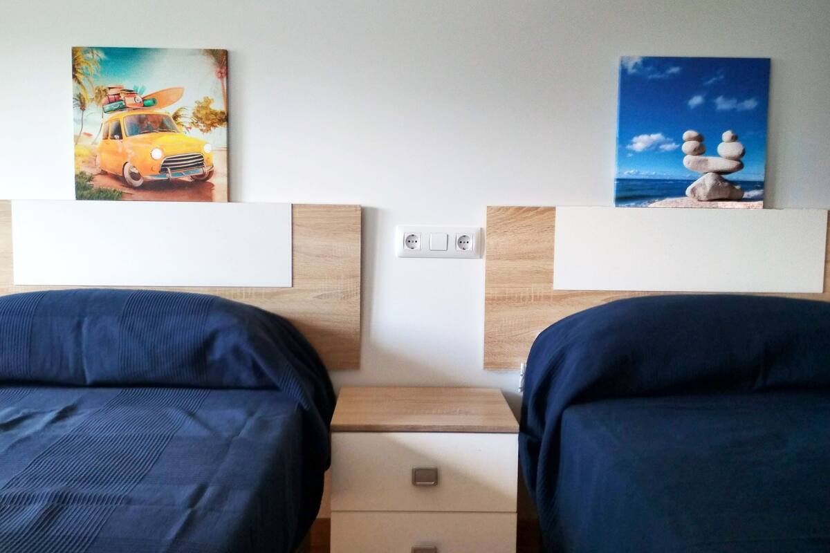A hotel room with two beds, a wooden headboard, and artwork depicting a car and a beach scene.