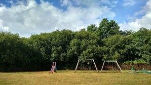 Un campo cubierto de césped con un parque infantil que incluye un tobogán y columpios.