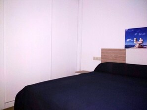 A bedroom with a bed, a wooden headboard, and a wall-mounted shelf with a painting. - Apartamentos Ares Centro 3000 (Ares)