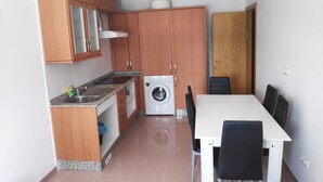 Cocina compacta con armarios de madera, lavadora integrada y comedor con mesa y sillas.