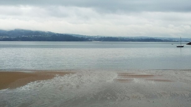 Vista amplia de una playa con mar tranquilo, un bote y una costa lejana.