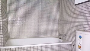 Un baño con una bañera blanca, un inodoro blanco y una pared con azulejos.