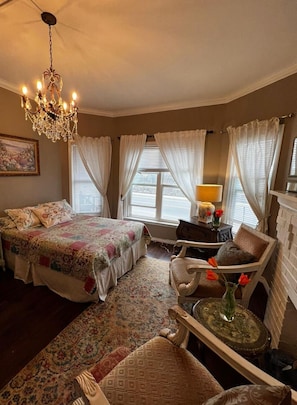 A bedroom with a large bed, a chandelier, a desk with a lamp, and a chair.
