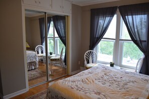 Une chambre à coucher avec un grand lit, un miroir, une chaise et une fenêtre avec des rideaux.