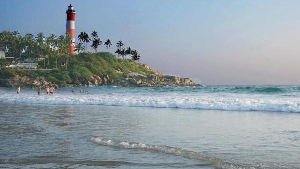 A beach with a lighthouse, palm trees, and rocky terrain. - Oceanbay Ayurvedic Beach Resort (Neyyattinkara)