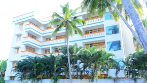 A multi-story building with balconies and a palm tree in front. - Oceanbay Ayurvedic Beach Resort (Neyyattinkara)