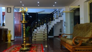 A lobby with a staircase, a brass lamp, a patterned sofa, and a red carpet. - Oceanbay Ayurvedic Beach Resort (Neyyattinkara)