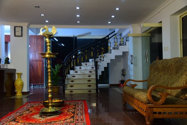 A lobby with a staircase, a brass lamp, a patterned sofa, and a red carpet.