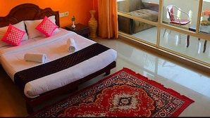 A hotel room with a large bed, a nightstand, a bedside lamp, a window with curtains, and a view of the outdoors. - Oceanbay Ayurvedic Beach Resort (Neyyattinkara)