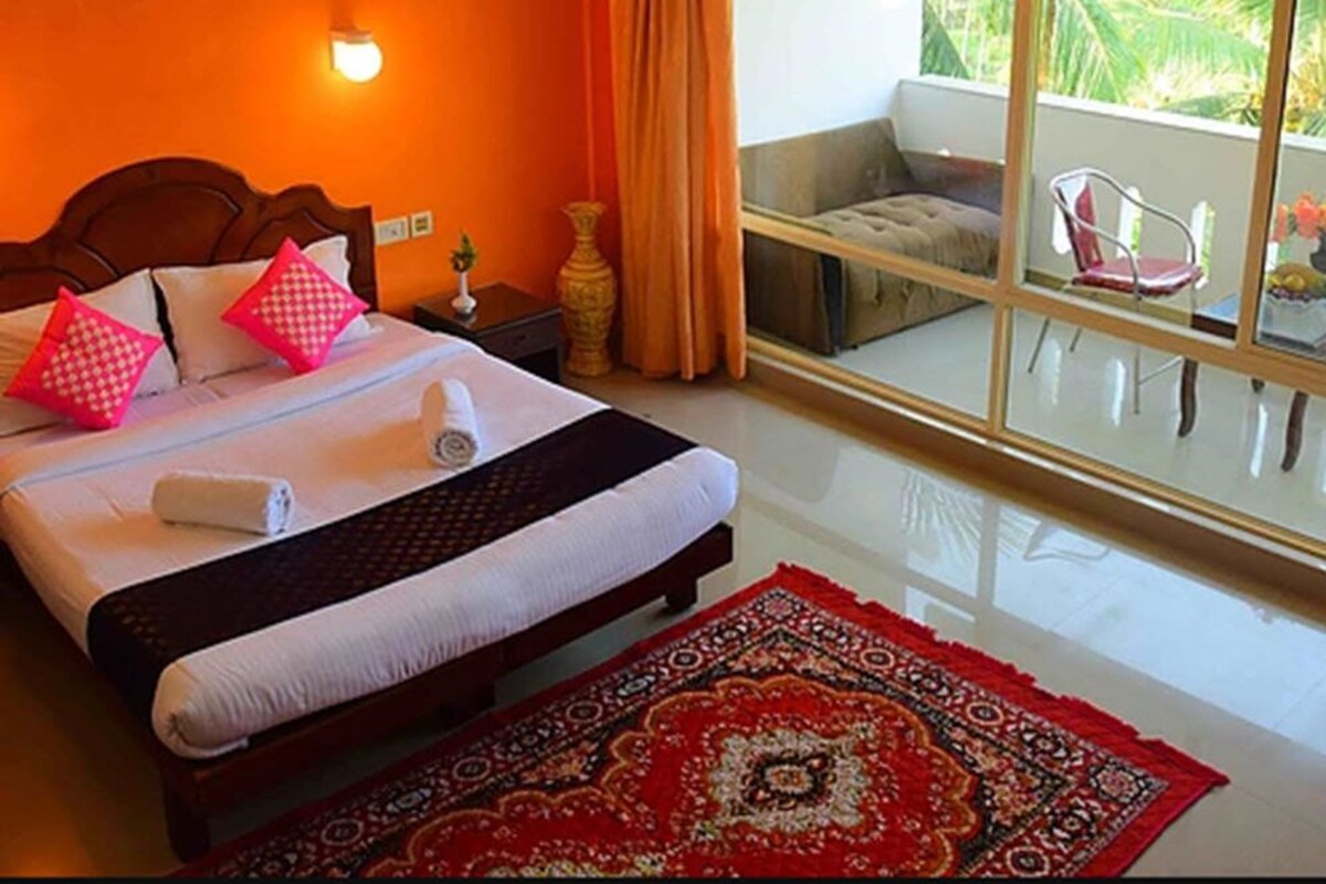 Ein Hotelzimmer mit einem großen Bett, einem Nachttisch, einer Nachttischlampe, einem Fenster mit Vorhängen und Blick ins Freie.